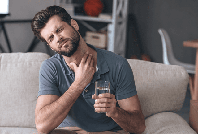 Man with a glass of water and looking uncomfortable from a sore throat